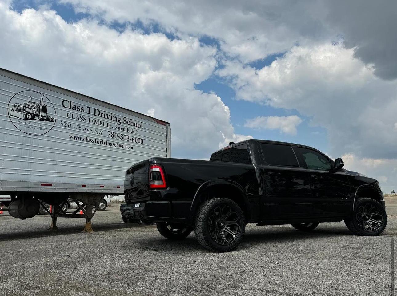 A black Ram pickup truck parked near a driving school trailer. The school offers Class 1 training.